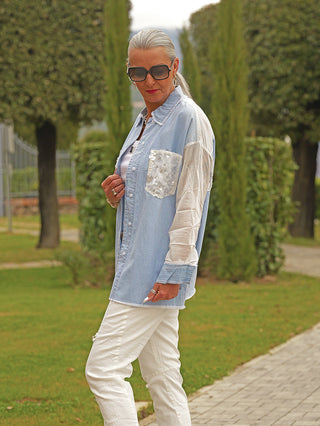 Reife Frau im Park trägt die OFF#DLY Denim Bluse Anna lightblue, mit transparenten Ärmeln und funkelnder Brusttasche, während sie auf einem gepflasterten Weg posiert.