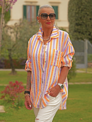 Mittelalterliche Frau trägt die OFF#DLY Bluse Dora white/stripe mit lockerer Passform, aufgerollten Ärmeln und lebendigem vertikalem Streifenmuster. Kombiniert mit weißen Hosen und silbernen Accessoires.