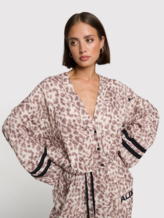 Frau trägt das ALIX Sporty Animal Jaclet, ein V-Ausschnitt-Jacke mit langen Batwing-Ärmeln, Leopardenmuster, schwarzen Knopfleiste, verstellbarem Taillenband und schwarzen Streifen an den Ärmelbündchen.