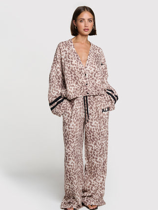 Frau trägt ALIX Sporty Animal Jaclet, eine lässige, kimono-inspirierte Jacke mit Leopardenmuster, V-Ausschnitt, langen Ärmeln mit schwarzen Streifen und aufgesetzten Taschen, kombiniert mit passenden Hosen.