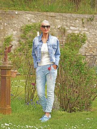 Frau trägt OFF#DLY Pant Denim Style Sola lightblue: lässige, crinkled Joggpant mit schmalem Schnitt und elastischem Bund, kombiniert mit Sneakern und einem weißen Top in einem Garten.