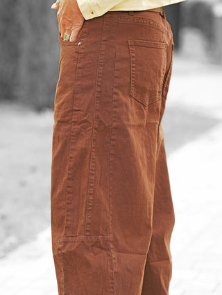 Nahaufnahme der OFF#DLY Barrel Color Denim Mia brown: rustfarbene, gerade geschnittene Hose mit sichtbaren Nähten, aufgesetzter Gesäßtasche und lässiger Barrel-Silhouette. Hand mit Ring in der Vordertasche.