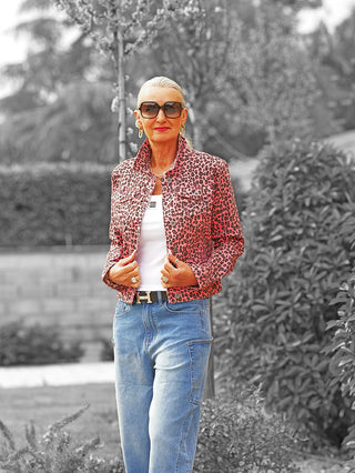 Frau im Garten mit der OFF#DLY Jacke Aice Leo Pink, einem pink-schwarzen Leoparden-Print-Denim, klassischer Schnitt mit Kragen und Knopfleiste, über weißem Tanktop und blauer Jeans.