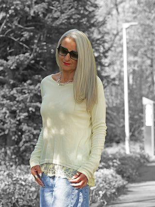 Mittelalte Frau trägt OFF#DLY LS Gloria butteryellow Longsleeve: zart, langärmelig, transparenter Stoff mit Spitzenkante, ideal für vielseitige Looks. Kombiniert mit blauer Jeans und silbernen Accessoires.