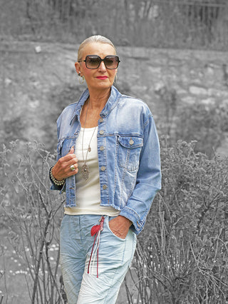 Frau trägt die OFF#DLY Jacke Sanna midblue, eine kurze Denim-Jacke mit Knopfleiste und Brusttaschen, kombiniert mit weißem Top und Accessoires, strahlt lässigen, modernen Stil aus.