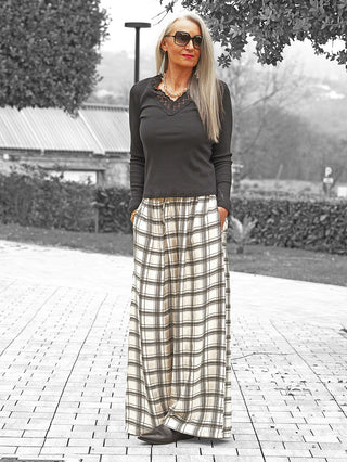 Frau in oversized Sonnenbrille und OFF#DLY Longsleeve Enie schwarz mit Spitzen-V-Ausschnitt, kombiniert mit weiten, karierten Hosen. Accessoires: Ohrhänger, Kette. Langer, glatter, silberblonder Haarstil.