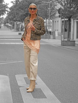 Frau in OFF#DLY Denim Style Jacke Leo mit trendigem Leo-Print und Jeansjacken-Schnitt, kombiniert mit Spitze und lockerer Hose, steht stilvoll auf einer ruhigen Stadtstraße.