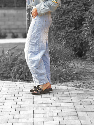Eine Person trägt die OFF#DLY Denim Barrel Denim Ela lightblue, eine lässige, weit geschnittene Jeans in heller Waschung, kombiniert mit schwarzen Sandalen und einem kurzen Jeansjacken-Saum sichtbar.