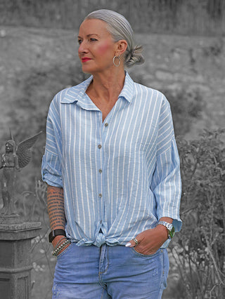 Mittelalterliche Frau trägt die OFF#DLY Bluse Sandra Stripes lightblue/white, ein locker geknotetes, leichtes Hemd mit vertikalen Streifen, kombiniert mit hellblauer Jeans.