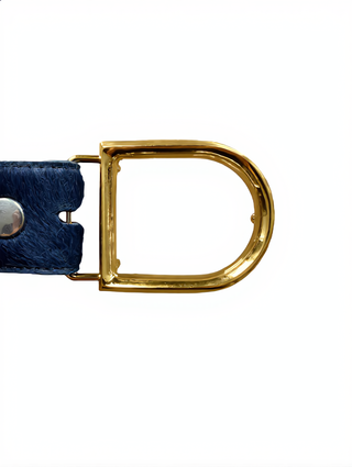 Nahaufnahme des UmjuBelt Circus gold: Ein goldfarbener D-Ring mit passendem rechteckigem Rahmen, befestigt an einem genoppten blauen Lederband, ideal für 4 cm breite Gürtel.