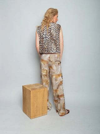 Emily Bluse 158402 Leo: Frau von hinten in ärmellosem Leo-Print-Top mit lockerer Passform und Bindebändchen am Ausschnitt, kombiniert mit weiten, gemusterten Hosen und flachen Sandalen.