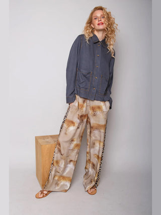 Frau in Emely Hose 201420 cognac leo, mit verschwommenem Leo-Print und Kontraststreifen, steht lässig; kombiniert mit grauem Hemd und flachen Sandalen.