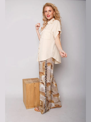 Frau trägt Emely Hose 201420 cognac leo: Weite, fließende Hose mit verschwommenem Leo-Print und kontrastierenden Streifen, kombiniert mit einer schlichten, kurzärmeligen Bluse für einen entspannten, modischen Look.