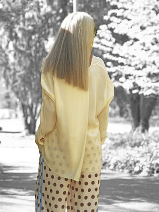 Eine Person trägt die Lumina Bluse Daniela creme, eine lockere, fließende, langärmelige Bluse mit verlängerter Rückenpartie, kombiniert mit weiten Hosen. Perfekt für elegante Sommerlooks.