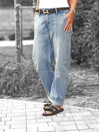 Person trägt OFF#DLY Denim Bea midblue Jeans mit lockerem Schnitt und umgeschlagenem Saum, kombiniert mit schwarzem Ledergürtel und flachen Sandalen, zeigt einen lässigen, modernen Street-Look.