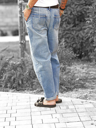 Person trägt OFF#DLY Denim Bea midblue, eine locker geschnittene Jeans mit umgeschlagenem Saum. Kombiniert mit schwarzen Sandalen, sichtbar sind auch Gürtel und Armbänder.