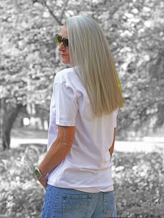 Person mit dem Rücken zur Kamera, trägt das OFF#DLY Tee Flora white, ein lässig geschnittenes, weißes T-Shirt mit auffälligem Frontprint und Nieten, kombiniert mit blauen Jeans.