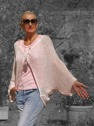 Frau trägt das OFF#DLY Netzoberteil Klara rosa über einem T-Shirt, kombiniert mit Jeans und Hamsa-Anhänger. Das locker gestrickte Design verleiht einen luftigen, modernen Boho-Look.