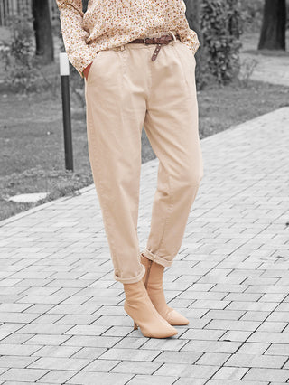 Person, trägt OFF#DLY Hose Amy beige mit umgeschlagenen Beinabschlüssen, kombiniert mit passendem Gürtel und beige Stiefeletten. Florales Oberteil leicht sichtbar, betont vielseitigen, lässigen Stil der Schlupfhose.