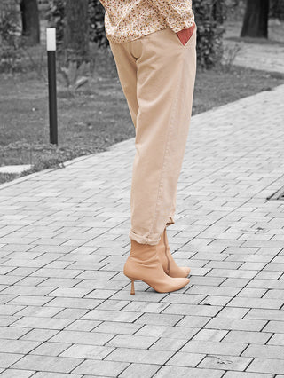 Die OFF#DLY Hose Amy beige zeigt einen entspannten, modernen Schnitt mit elastischem Bund und Gürtel, getragen mit eleganten, spitzen Stiefeletten auf einem gepflasterten Weg.