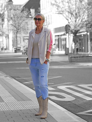 Frau trägt die OFF#DLY Denim Milano lightblue Jeans mit modernem Used-Look und leichtem Destroy-Effekt, kombiniert mit cremefarbenem Blazer und Westernstiefeln, für einen lässigen, stilvollen Straßenlook.