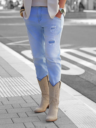 OFF#DLY Denim Milano lightblue Jeans mit leichtem Used-Look, getragen mit beige Cowboy-Stiefeln. Die Jeans sitzt figurbetont, leicht gestreckt, und zeigt moderne Risse für einen lässigen, stylischen Auftritt.