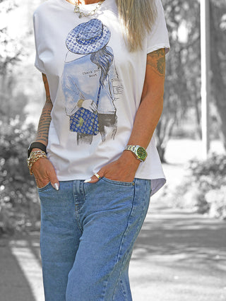 „OFF#DLY Tee Hat white/blue“ zeigt eine Person in lockerer Passform mit auffälligem Fashion-Print einer Frau im Hut. Kombiniert mit Jeans, Schmuck und Tätowierungen für einen trendigen Casual-Look.