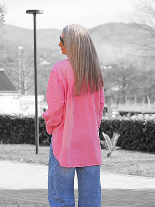 Person trägt die OFF#DLY Bluse Anna pink im Oversize-Stil, mit langen Ärmeln und strukturierter Brusttasche, kombiniert mit hellblauen Jeans, im Freien stehend mit den Händen in den Taschen.