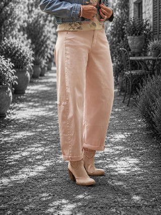 Person trägt OFF#DLY Pant Ronja rosa, eine hochgeschnittene, weite Hose in sanftem Rosé, kombiniert mit floralem Oberteil und Jeansjacke, auf einem sonnigen Weg.