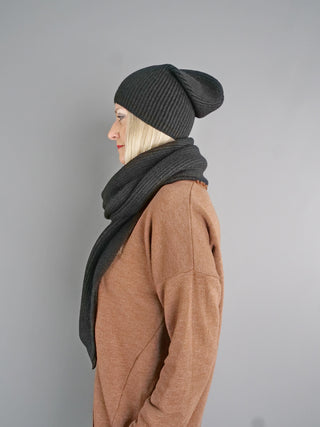 Seitenansicht einer Person mit OFF#DLY Schal schwarz um den Hals. Der Schal ergänzt das Outfit, drapiert elegant über die Vorderseite, getragen mit einem dunklen, gerippten Beanie und warmem Pullover.