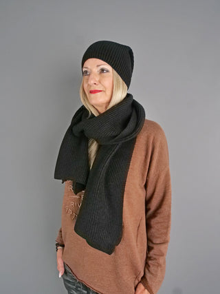 Frau trägt einen schwarzen, gerippten OFF#DLY Schal schwarz um den Hals, kombiniert mit einem passenden Beanie. Der Schal ist lang und locker drapiert, ideal für kaltes Wetter.