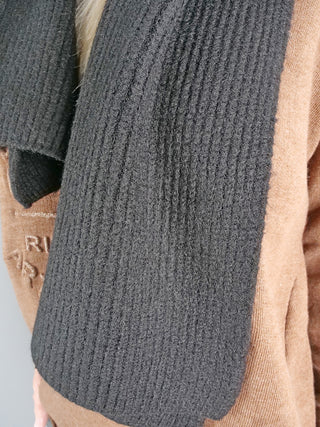 Nahaufnahme eines weichen, gerippten OFF#DLY Schal schwarz, getragen über einem hellbraunen Pullover mit gesticktem Schriftzug. Der Schal ist kuschelweich und funktional, ideal für kalte Tage.