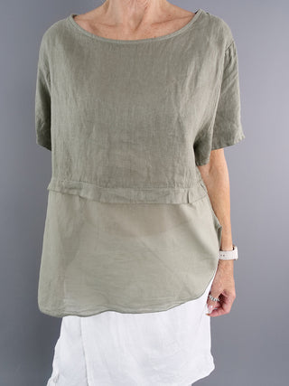Person trägt das OFF#DLY Shirt in Khaki, ein kastig geschnittenes, atmungsaktives Cropped-Shirt mit kurzen Ärmeln, das aus einem leichten Baumwoll-Leinen-Mix gefertigt ist.