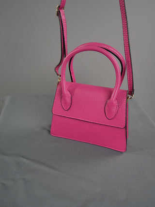 OFF#DLY Ledertasche pink aus 100% Leder mit Tragehenkeln und Riemen, präsentiert auf grauer Oberfläche, Größe 20x18x7 cm.