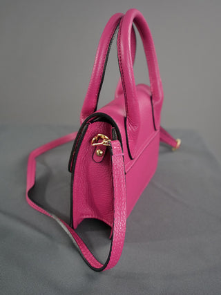 OFF#DLY Ledertasche pink mit schwarzen Akzenten, aus 100% Leder, auf grauer Fläche. Inklusive Tragehenkel und Riemen, Größe 20x18x7 cm.