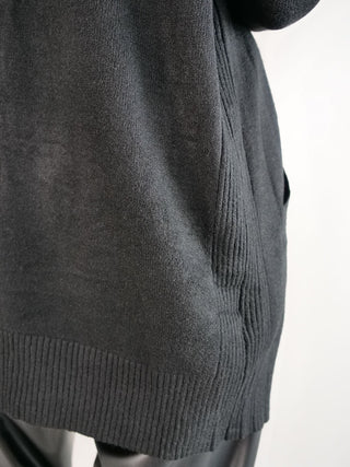 Nahaufnahme der OFF#DLY Strickjacke mit Kapuze schwarz, zeigt den gerippten Saum, die Seitentasche und darunter dunkle Leggings, die vermutlich an einer Schaufensterpuppe getragen werden.