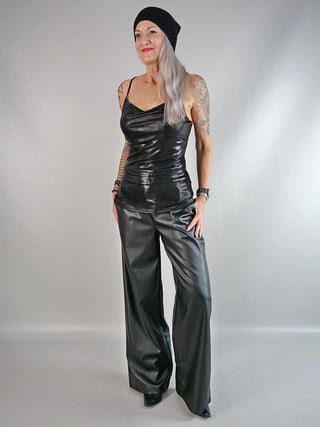 OFF#DLY Top Black metallic: Frau trägt ein schwarzes Metallic-Glitzer-Top mit Spaghetti-Trägern und elegantem Ausschnitt, ideal für glamouröse Anlässe. Passend zu schlichten schwarzen Hosen und Beanie.