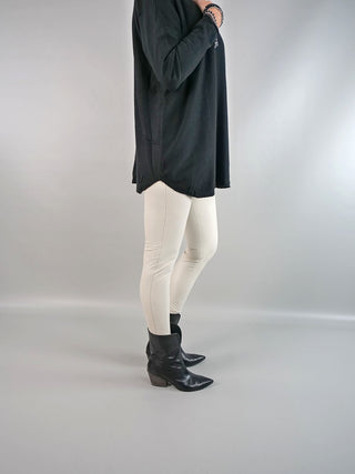 Eine Person trägt die OFF#DLY Legging Creme, kombiniert mit schwarzen Stiefeln. Die Legging ist aus 100% Polyester und bietet eine schlichte, moderne Silhouette.