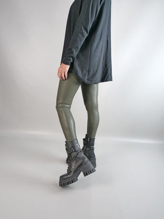 Person trägt die OFF#DLY Fake Leder Legging khaki mit schwarzen Stiefeln, betont durch eng anliegendes Design und glattes Finish, ideal für modische Outfits.