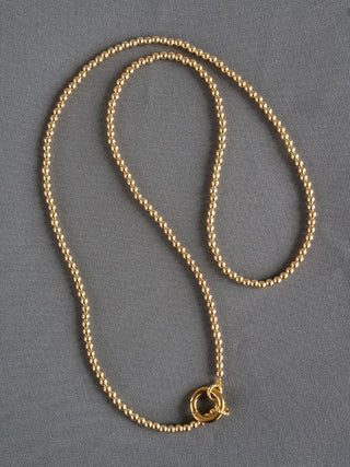 Goldene Kugelkette schmal aus Edelstahl, präsentiert auf grauer Oberfläche. Die Kette ist 100cm lang mit 3mm Kugeldurchmesser, ideal als elegantes Modeaccessoire.
