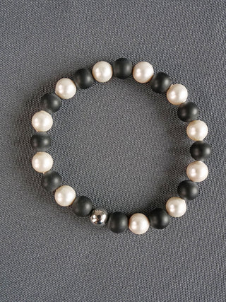 Armand Onyx Perle 1/1, ein Armband mit schwarzen Onyx- und weißen Süßwasserperlen, präsentiert elegantes Design als modisches Accessoire. Perlendurchmesser beträgt 6 mm.