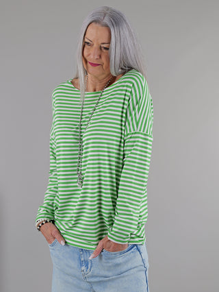 OFF#DLY Ringelshirt green/white: Frau mit grauen Haaren trägt ein gestreiftes Langarmshirt mit Rundhalsausschnitt, kombiniert mit blauen Jeans. Ihr Arm steckt in einer Tasche, ein Armband sichtbar.