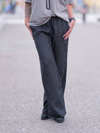 Gitta Banko Hose Alina: Eine Person trägt eine lässige, leichte Leinenhose. Sichtbar sind graue Pants, ein Armband und Schuhe. Die Hose fällt etwas größer aus und besteht aus 100% Leinen.