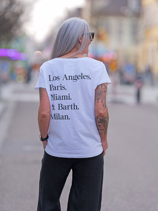 Frau mit Tattoos trägt das ONE TEE Lisa white aus 100% Baumwolle. Sie hat graue Haare, kombiniert das Shirt mit schwarzen Hosen, zeigt Street-Fashion-Stil.