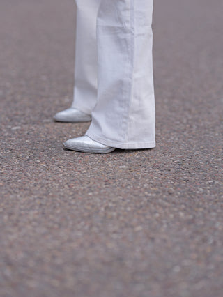 Person trägt OFF#DLY Wide Leg Denim Romina, weiße weite Hose, kombiniert mit silbernen Schuhen. Ideal für lässigen, modernen Look. Passform zeigt bequemes Design mit modischem Flair.