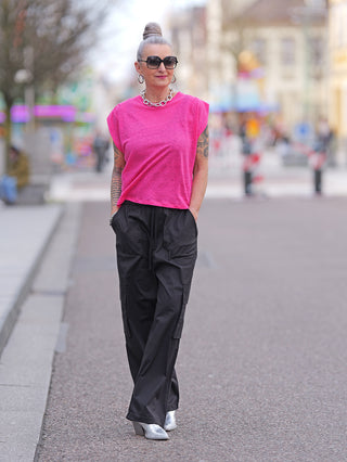 LTC Tee Muflier fuchsia: Frau trägt ein lässiges, oversized Leinen-T-Shirt mit angeschnittenen Ärmeln und Strass-Schriftzug Cerises auf dem Rücken. Kombiniert mit schwarzer Hose und Sonnenbrille.