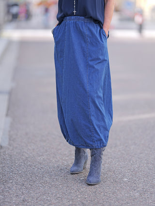 Frau trägt langen blauen OFF#DLY Rock Julietta mit Gummizug und grauen Stiefeln, passend für lässige Straßenmode. Ideal für ein entspanntes, stilvolles Outfit.