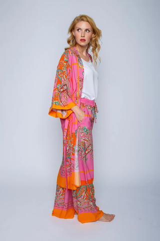 Emily Hose Pink Orange, getragen von einem Modell. Die Hose hat ein elastisches Bündchen und Bindeband, seitliche Eingriffstaschen und ein buntes Paisley-Muster. Geeignet für moderne Sommermode.