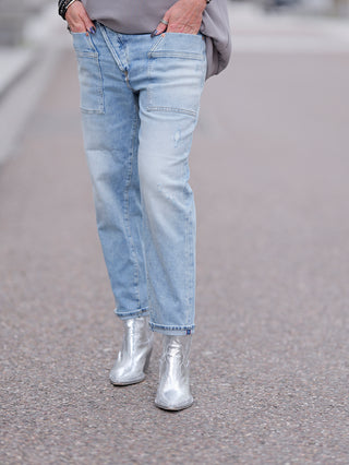 LTC Jean Femme Cosy Pochet, getragen von einer Person mit silbernen Stiefeln, zeigt einen lockeren Schnitt aus dehnbarem Candiani-Denim mit normaler Taille und Knopfverschluss.