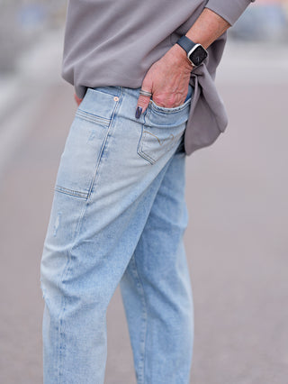 Eine Person trägt die LTC Jean Femme Cosy Pochet, mit einer Hand in der Tasche und einer Armbanduhr sichtbar. Die Jeans hat eine lockere Passform und normale Taillenhöhe.